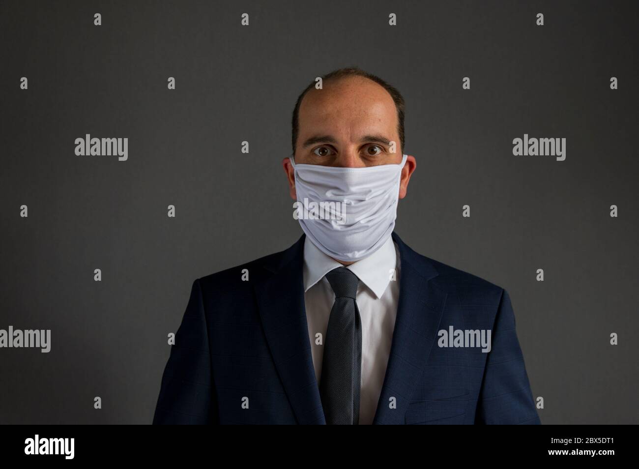 ritratto di un uomo d'affari vestito con abito e cravatta con una maschera protettiva guarda nella fotocamera. Sfondo grigio con un sacco di copia spa Foto Stock