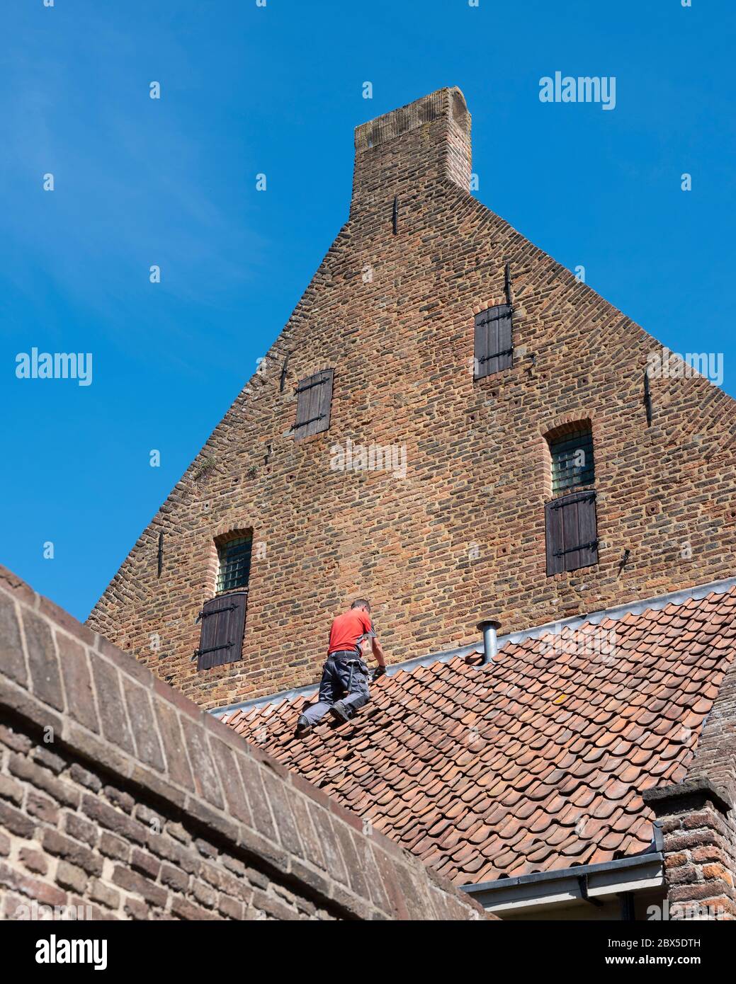 uomo in camicia rossa ripara l'edificio medievale nel centro storico di zutphen, nei paesi bassi Foto Stock
