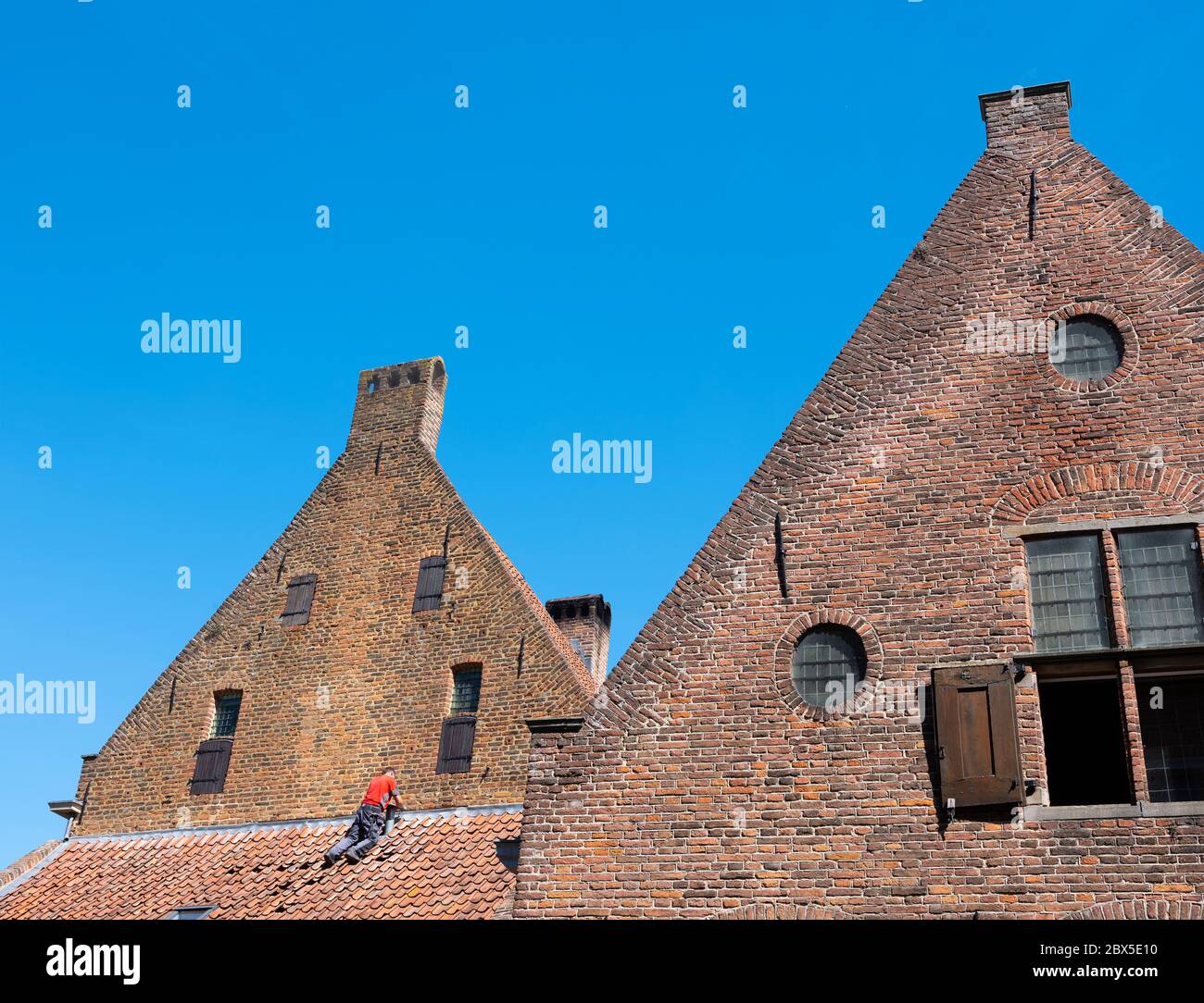 uomo in camicia rossa ripara l'edificio medievale nel centro storico di zutphen, nei paesi bassi Foto Stock