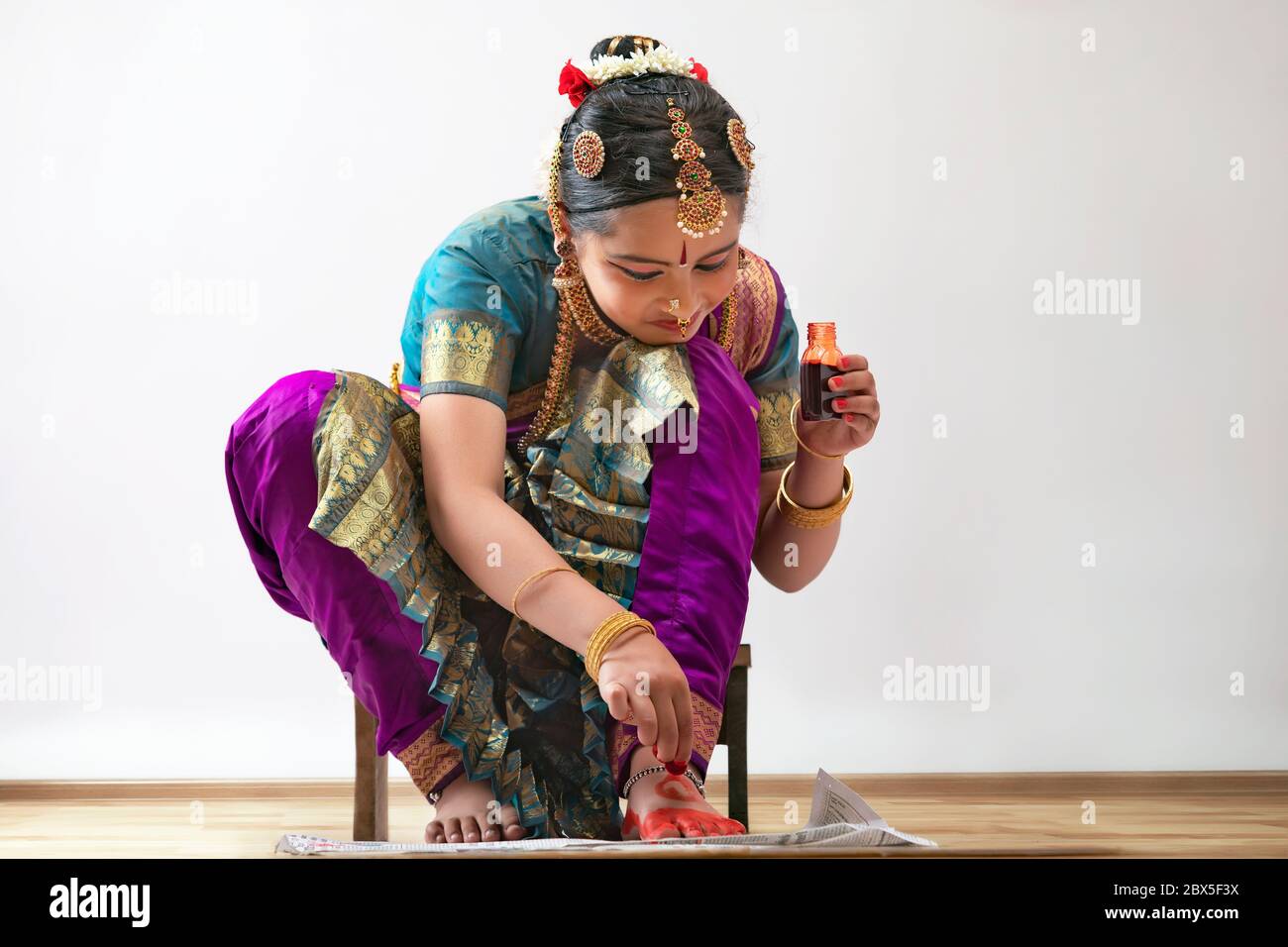 Giovane bharatnatyam ballerina seduta e applicando alta sui suoi piedi. Foto Stock