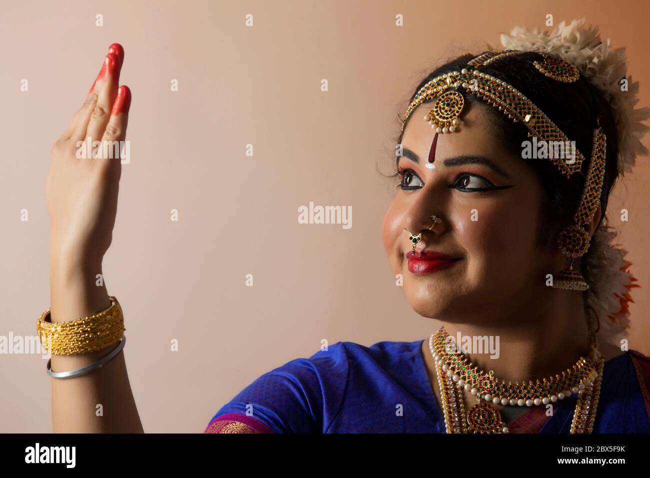 Ballerina di Bharatnatyam che guarda la sua palma mentre si trova di fronte ad uno sfondo piano. Foto Stock