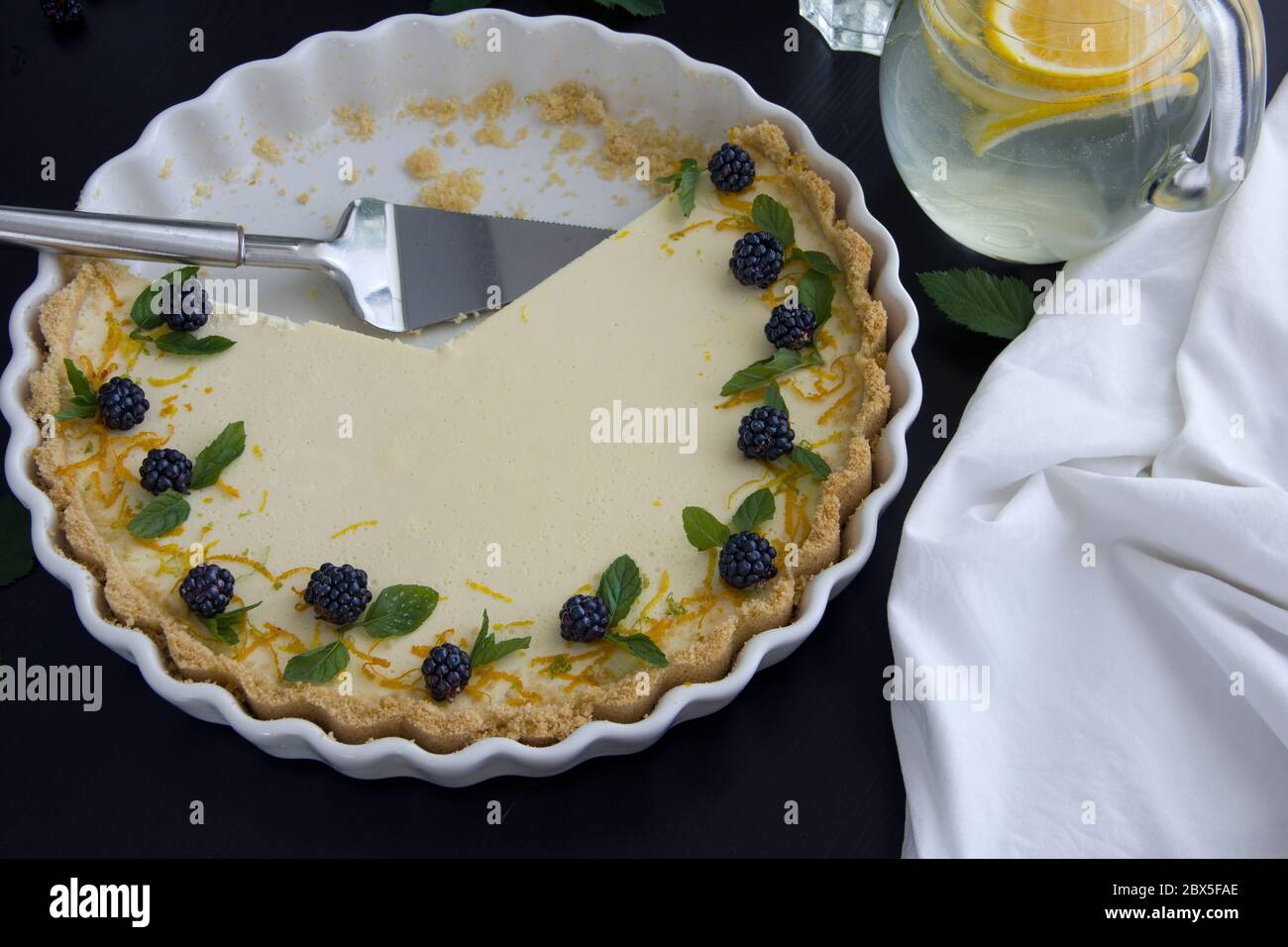 Cheesecake al limone fatto in casa in una teglia bianca in ceramica. Fetta di torta di limone su un piatto da portata bianco, tazza di tè bianco Foto Stock