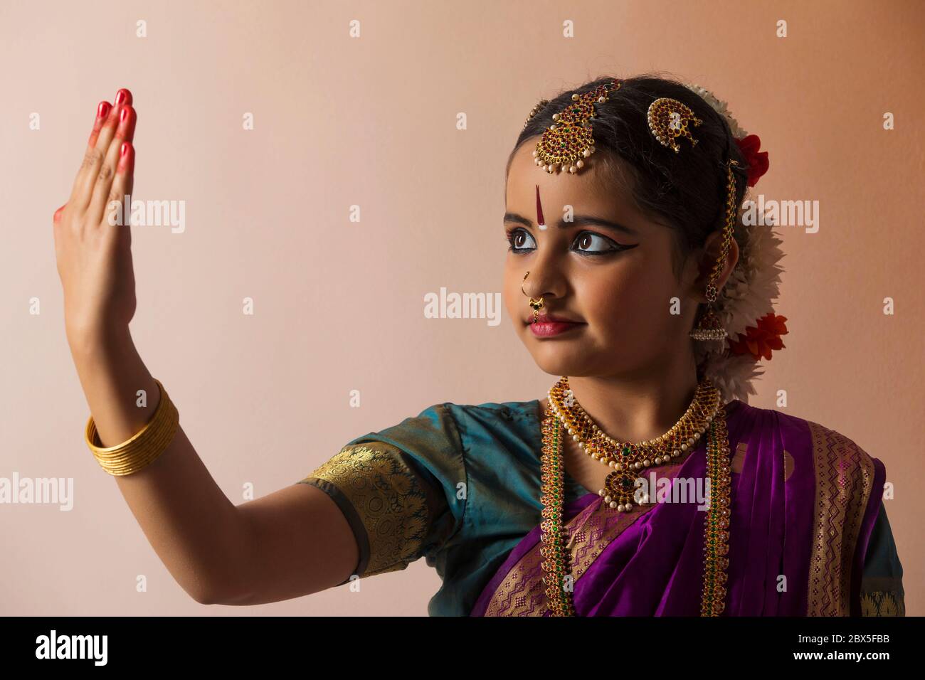 Giovane bharatnatyam ballerina con grazia guardando la sua palma di fronte ad uno sfondo piano. Foto Stock