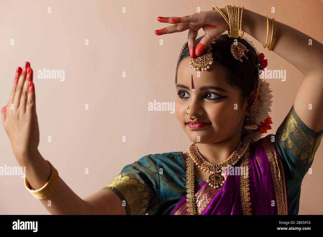 Giovane bharatnatyam ballerina con grazia guardando la sua palma di fronte ad uno sfondo piano. Foto Stock