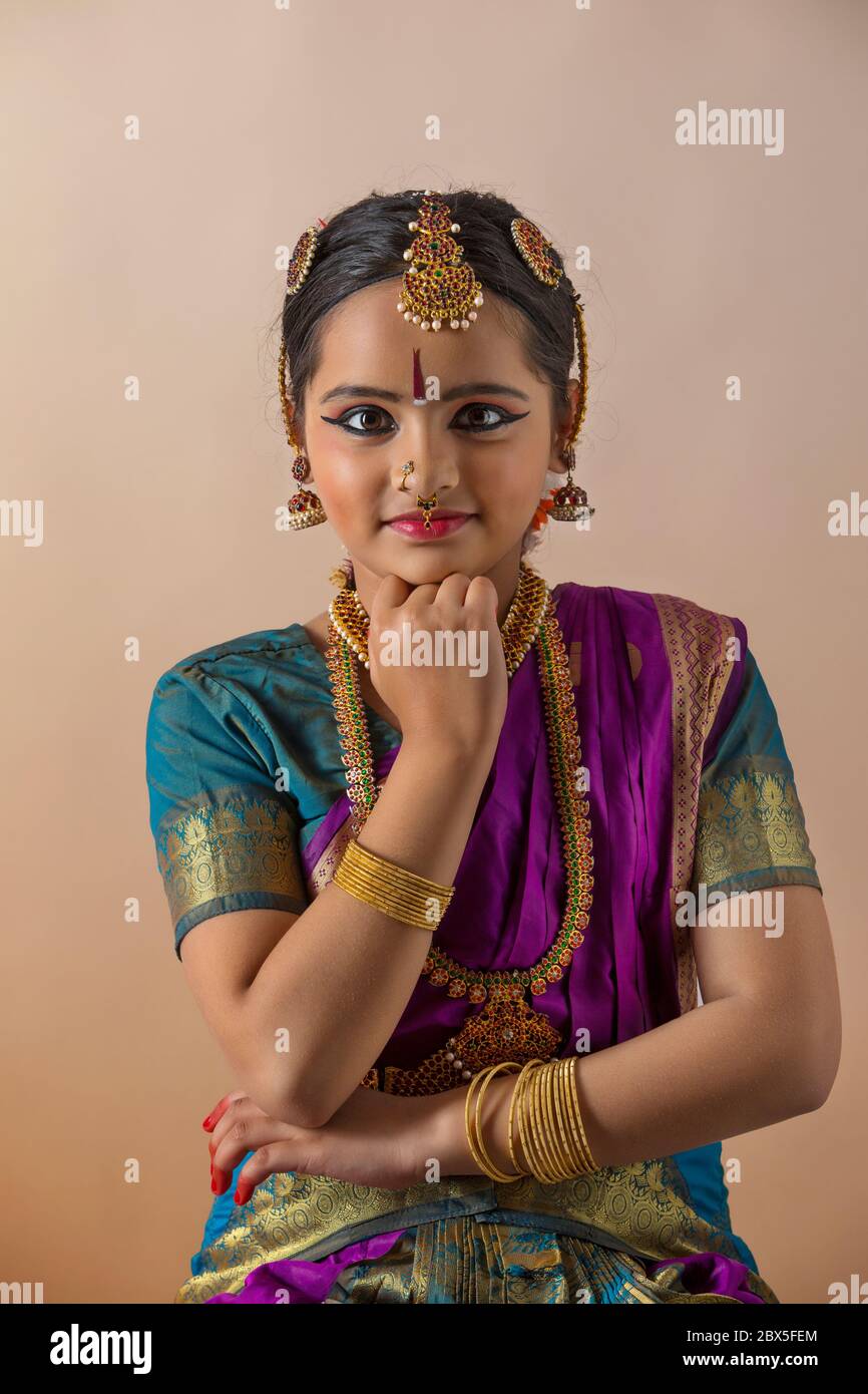 Giovane bharatnatyam ballerino in piedi con grazia davanti ad uno sfondo piano e sorridente. Foto Stock