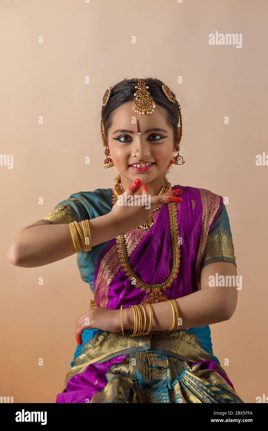 Giovane bharatnatyam ballerino in piedi con grazia davanti ad uno sfondo piano e sorridente. Foto Stock