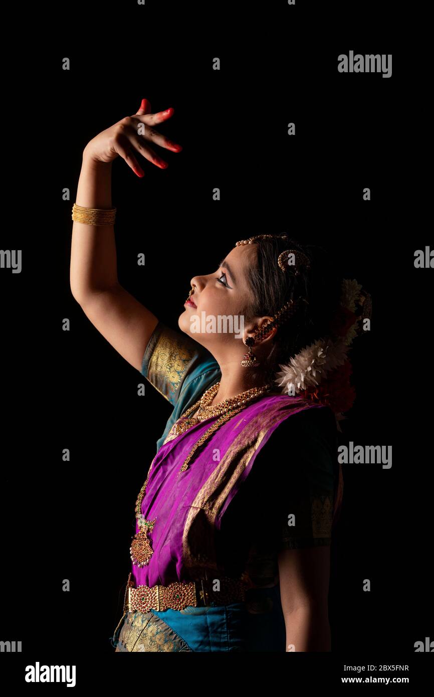 Giovane ballerina bharatnatyam che offre una performance affascinante davanti a uno sfondo scuro. Foto Stock