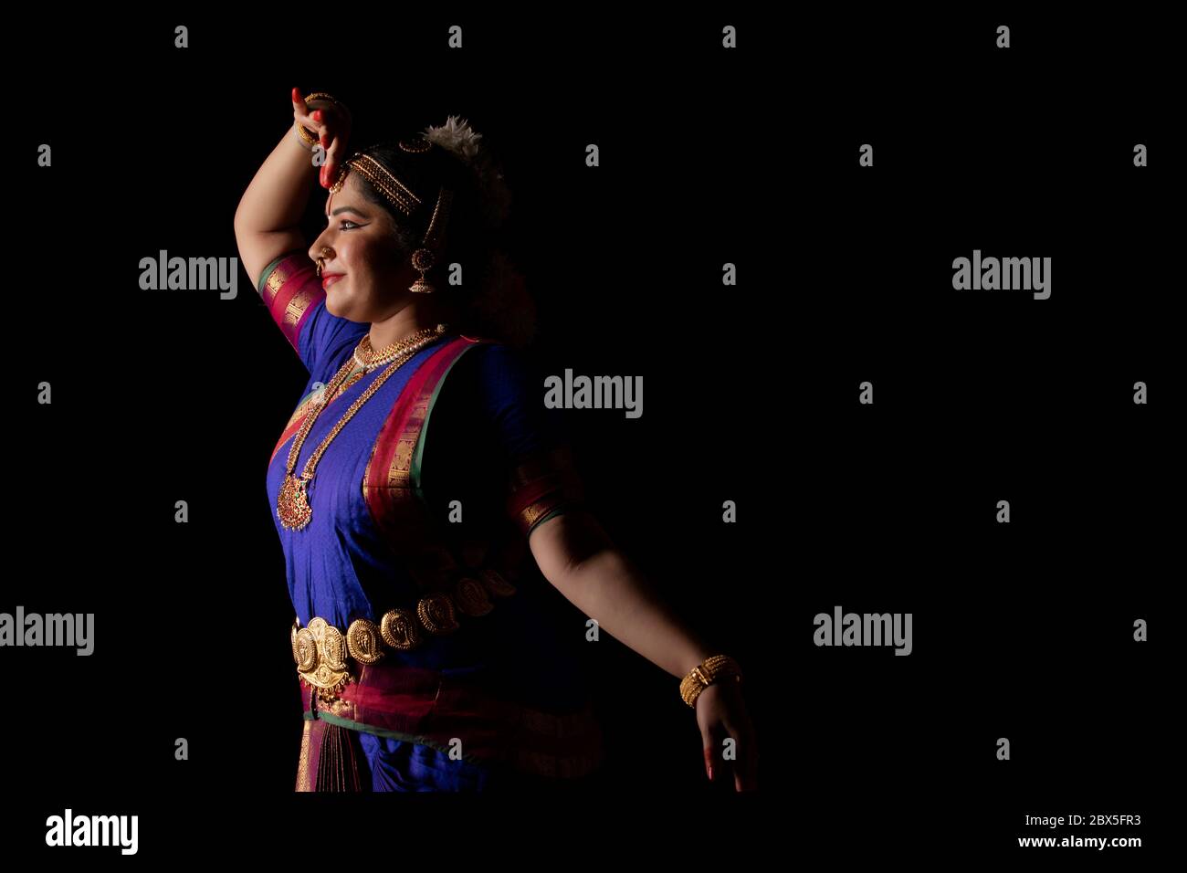 Ballerina Bharatnatyam che offre una performance affascinante davanti a uno sfondo scuro. Foto Stock