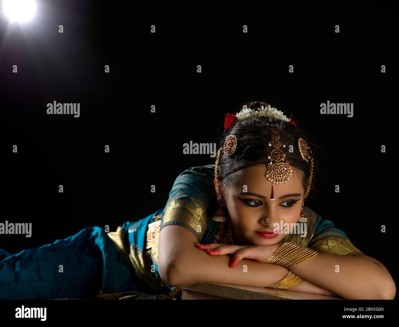 Giovane ballerina bharatnatyam riposante con grazia su uno sfondo scuro. Foto Stock