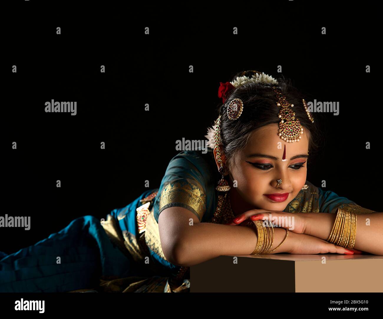 Giovane ballerina bharatnatyam riposante con grazia su uno sfondo scuro. Foto Stock
