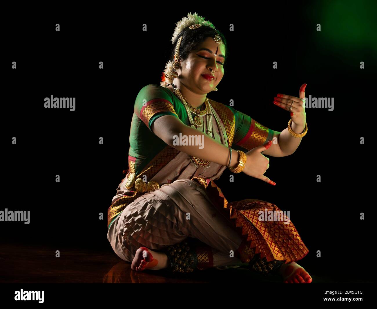 Ballerina Bharatnatyam seduta di fronte a uno sfondo scuro e spettacolo. Foto Stock