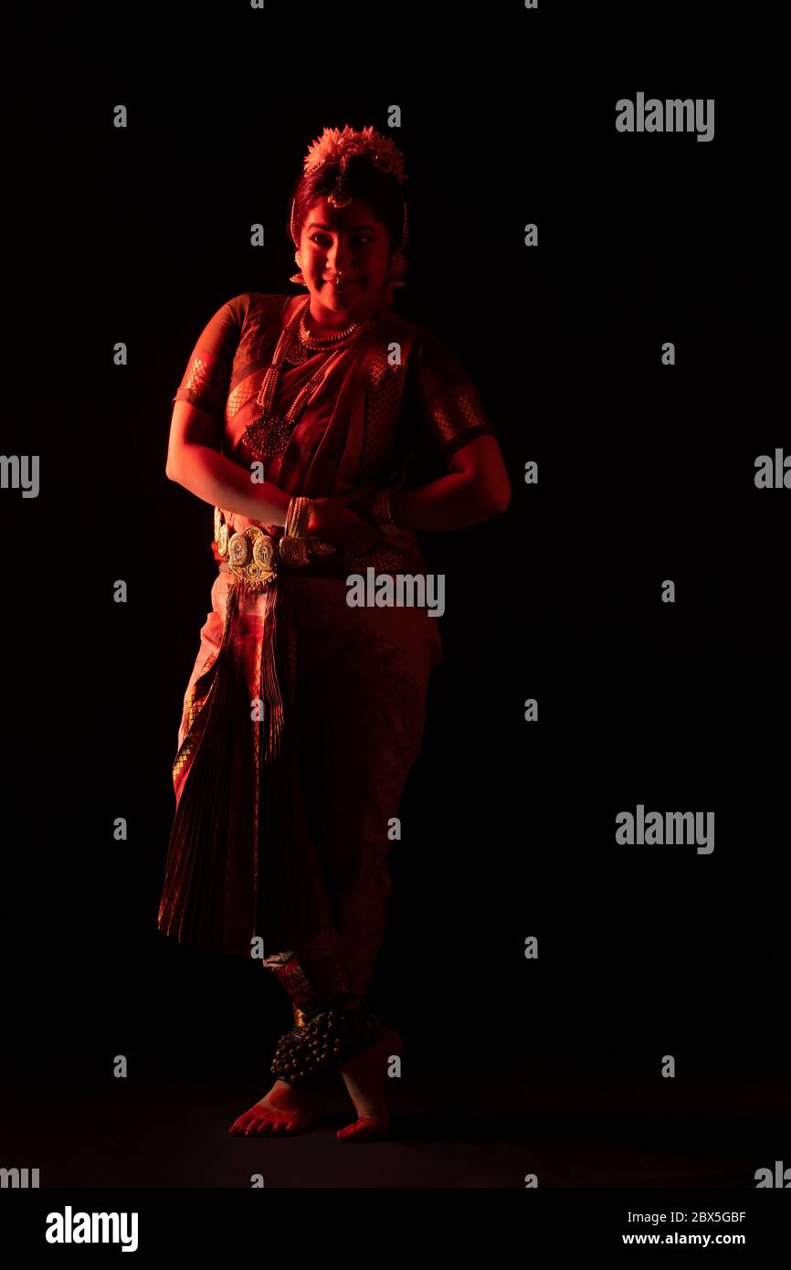 Ballerina Bharatnatyam in piedi con grazia davanti a uno sfondo scuro. Foto Stock