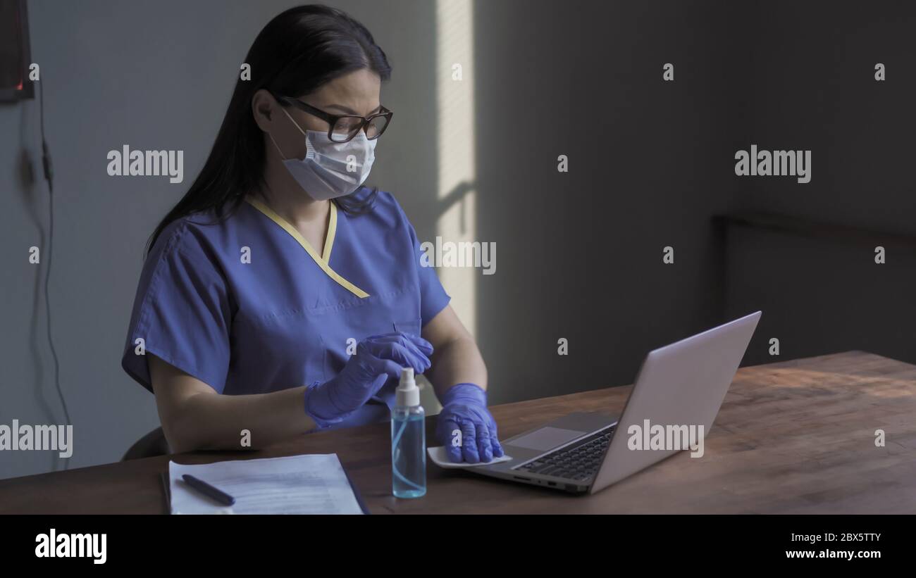 Il medico pulisce con un panno la tastiera del computer. Donna pulisce la superficie di lavoro con un liquido disinfettante o una soluzione. Concetto di disinfezione. Virus Foto Stock