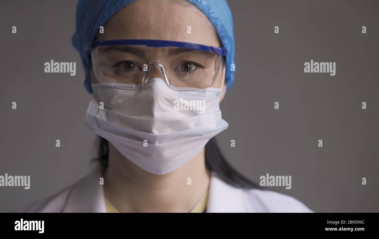 Medico stanco su sfondo grigio. Donna asiatica guardando la macchina fotografica. Immagine sfocata astratta in movimento Foto Stock