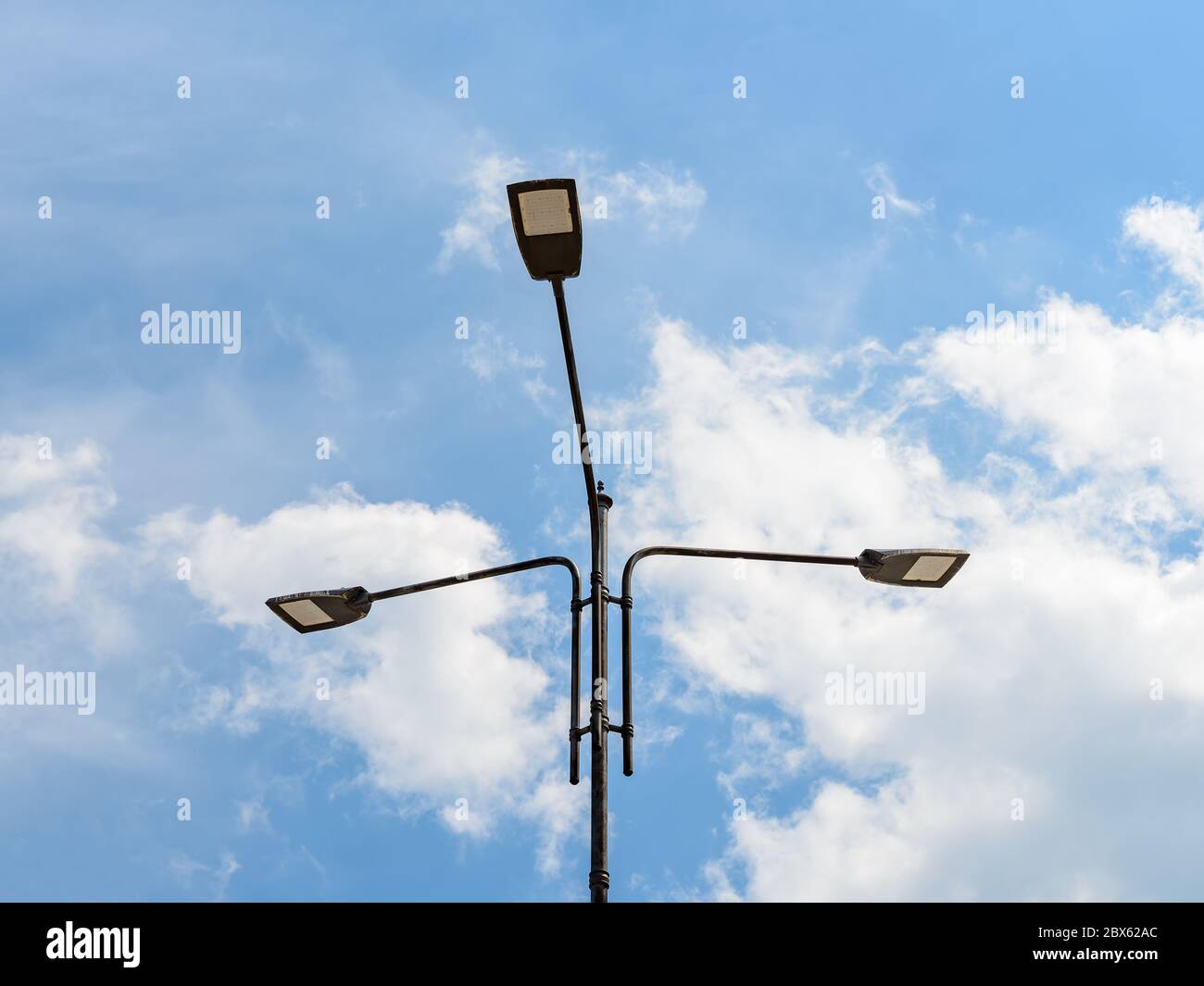 Tre luci a LED su un palo contro il cielo blu con nuvole chiare. Moderna  tecnologia a risparmio energetico per l'illuminazione di strade e strade.  Lampada da strada a LED Foto stock -