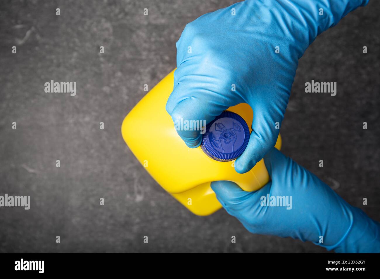 Mano umana in un guanto protettivo che apre un flacone di candeggina giallo. Concetto di disinfezione Foto Stock