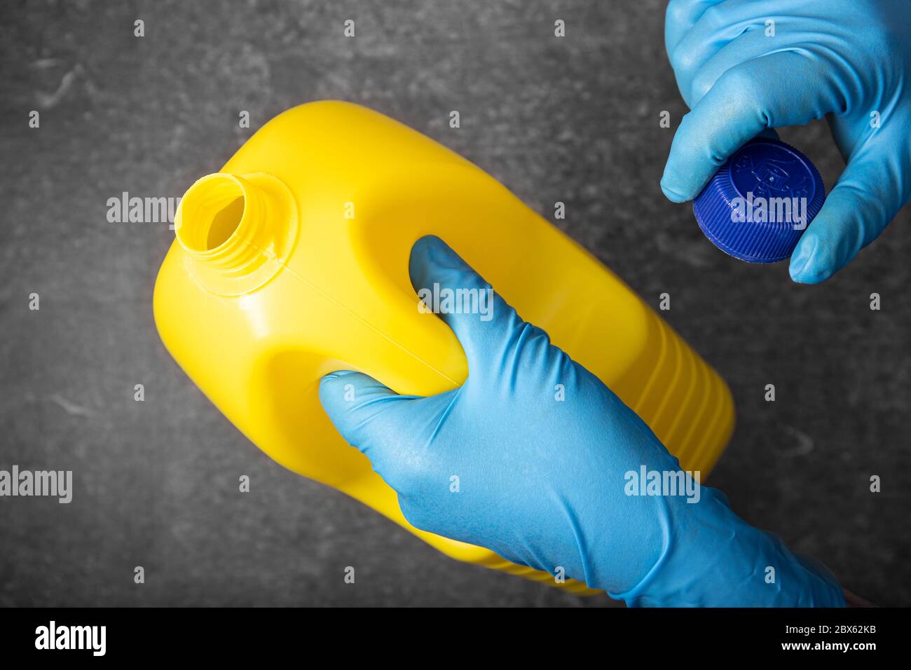 Mano umana in un guanto protettivo che contiene un flacone di candeggina giallo. Concetto di disinfezione Foto Stock