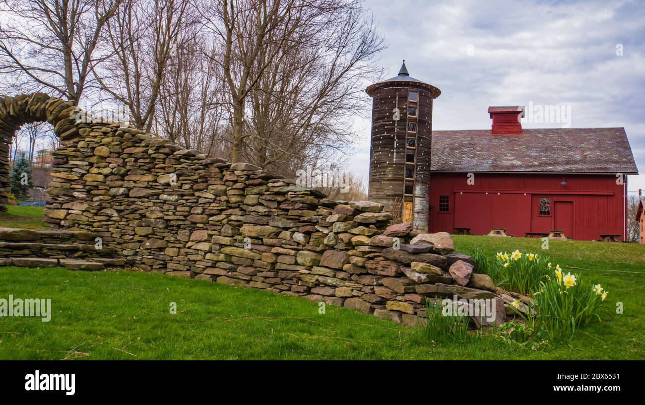 una vista attraverso un arco di pietra di silo rotondo storico restaurato e fienile rosso in primavera Foto Stock