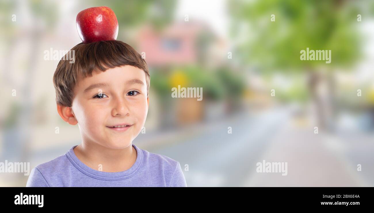 Bambino ragazzo con mela rossa frutta sulla sua testa città banner copyspace copia spazio sano mangiare concetto all'aperto Foto Stock