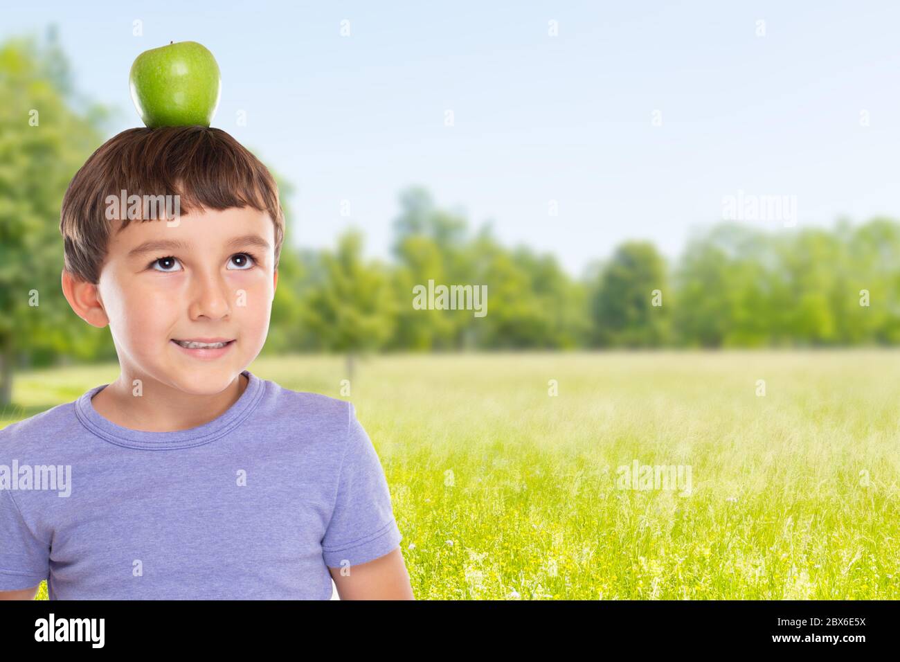 Bambino giovane con una frutta di mela sulla sua testa all'aperto copyspace copia spazio mangiare sano all'esterno Foto Stock