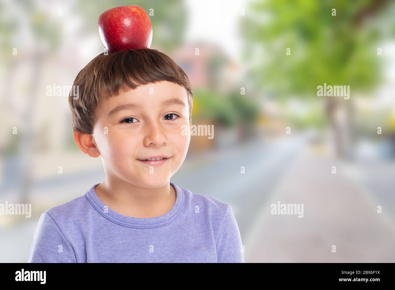 Bambino giovane con mela rossa frutta sulla sua testa città copyspace copia spazio sano mangiare concetto all'aperto Foto Stock