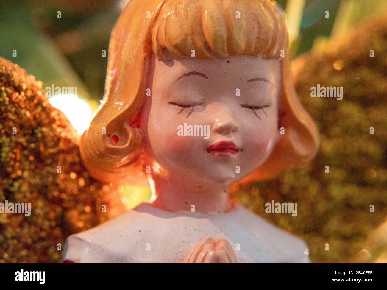 Albero di Natale ornamento di un bambino blonde femmina Angelo chiusura I suoi occhi in preghiera con l'albero di Natale e le luci offuscate In background Foto Stock