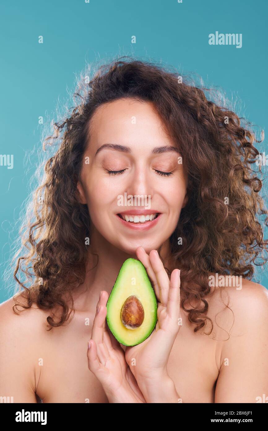 Felice giovane donna di lusso con bianco sorriso toothy tenendo metà di fresco avocado che la aiuta a prendersi cura della pelle e del corpo Foto Stock