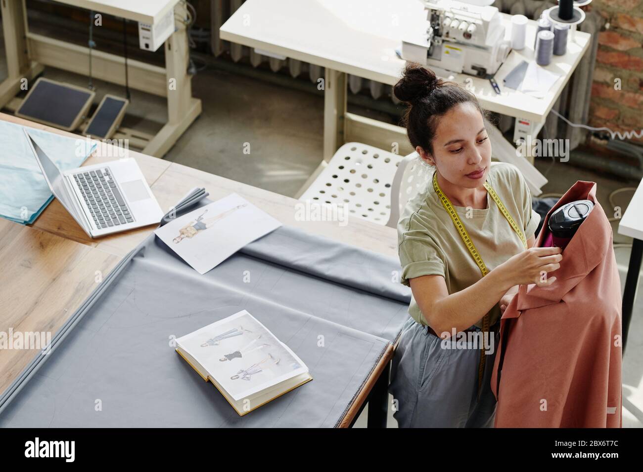 Giovane lavoratore moderno di moda studio di cucire articoli di abbigliamento su manichino mentre lavorando su nuova collezione stagionale in officina Foto Stock