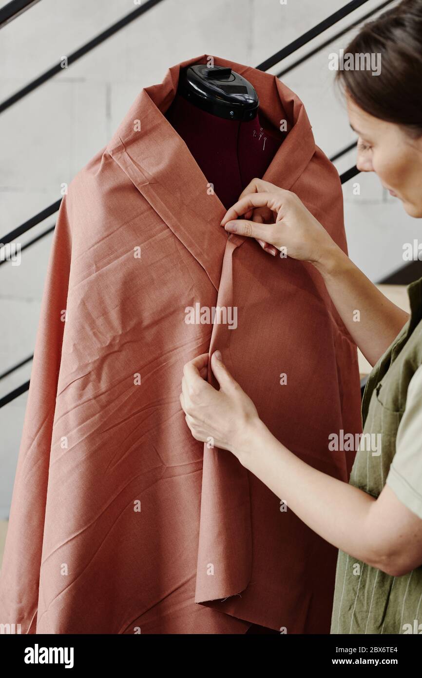 Giovane marinaio in piedi da manichino avvolto in un pezzo di stoffa marrone e cucire i suoi bordi prima di cucire nuovo articolo sulla macchina Foto Stock