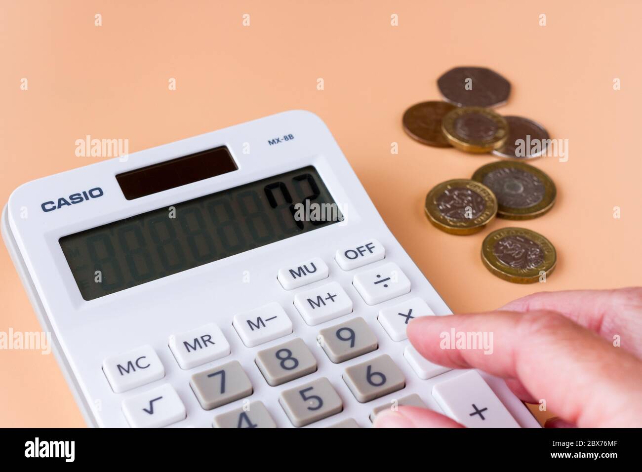 Una calcolatrice e alcune monete britanniche. Concetto di budget per le famiglie. Foto Stock