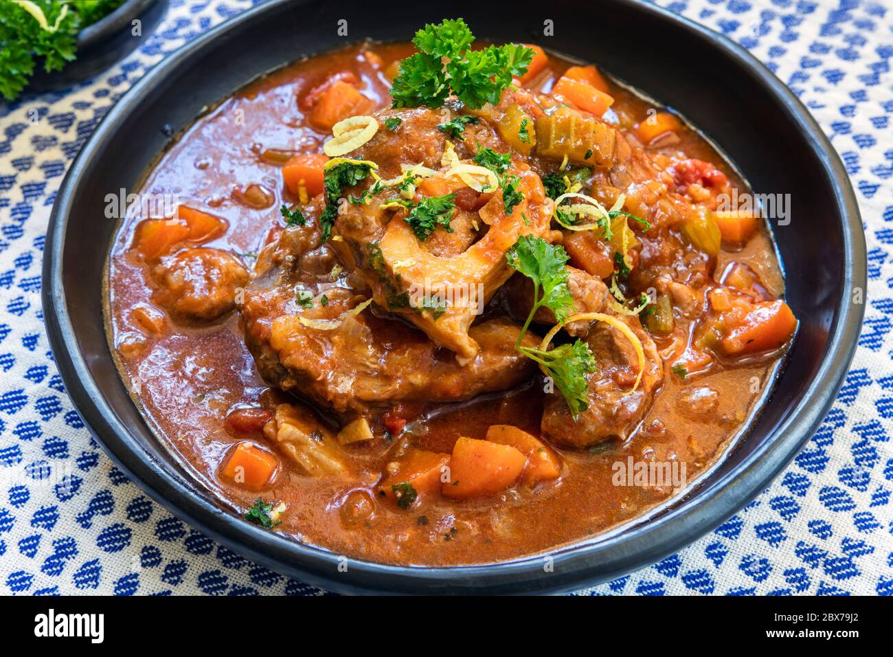 Casseruola di vitello Osso Buco con gremolata, in ciotola nera rustica. Foto Stock
