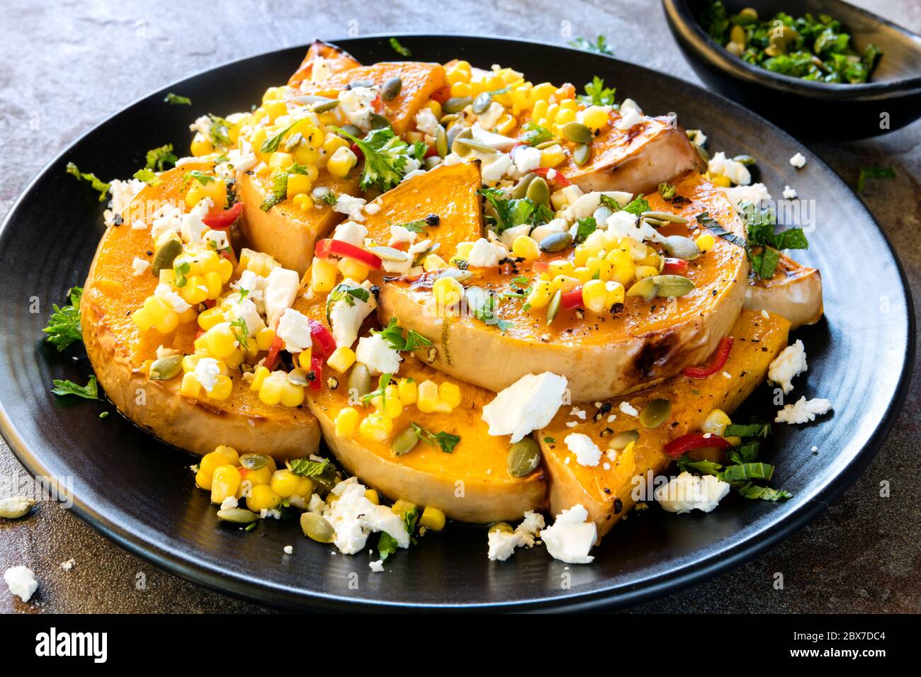 Insalata di zucca o zucca arrosto, con salsa al peperoncino e mais, formaggio feta e pepitas. Condito con menta. Foto Stock