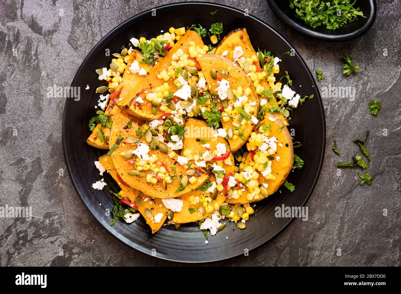Zucca arrosto o zucca con un mais dolce e peperoncino sasa, formaggio feta e pepitas. Con menta fresca. Vista dall'alto su ardesia. Foto Stock