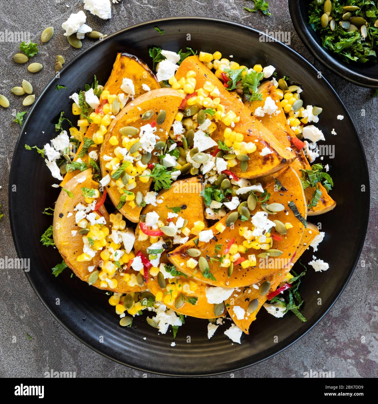 Zucca arrosto o zucca con un mais dolce e peperoncino sasa, formaggio feta e pepitas. Con menta fresca. Vista dall'alto su ardesia. Foto Stock