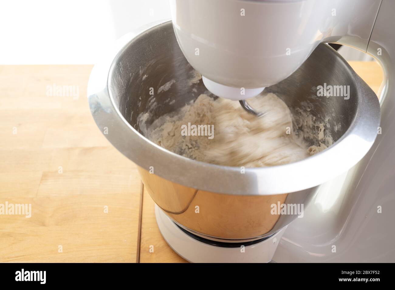 Il mixer in azione sta mescolando l'impasto con il gancio in una ciotola in acciaio inox su un'area di lavoro in legno, sfocatura movimento, spazio copia, selezionato Foto Stock