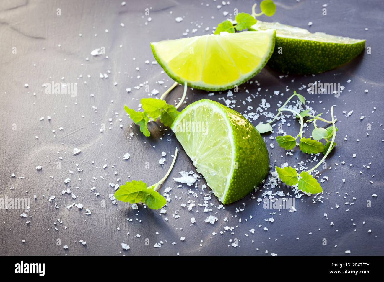 Spicchi di lime con sale marino e micro erbe, oltre di ardesia scura. Foto Stock