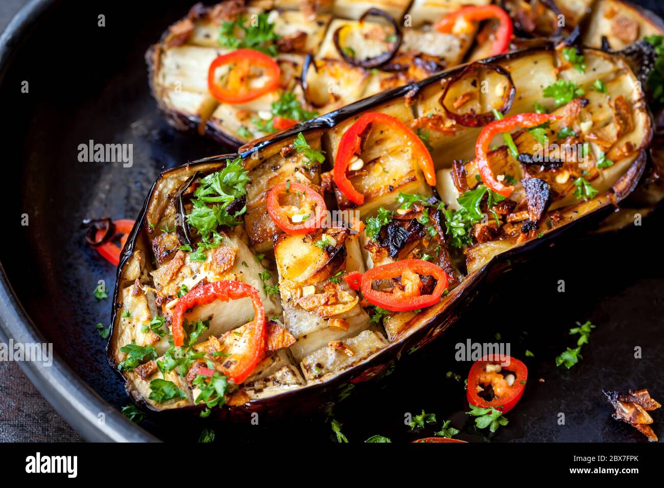 Melanzane arrosto farcite con aglio e peperoncino, in rustico piatto nero. Foto Stock