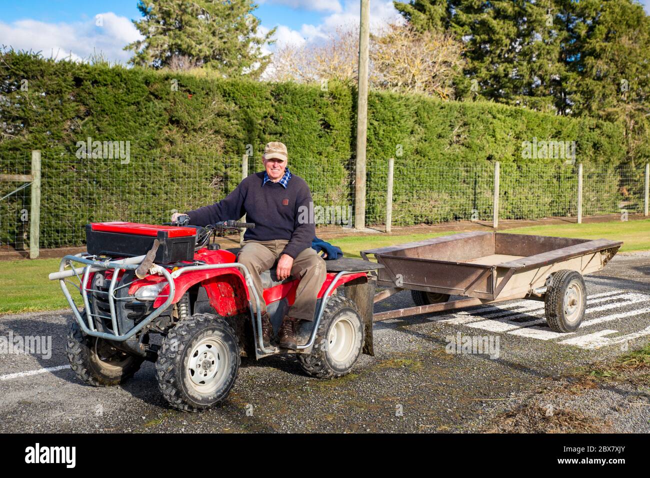 Annat, Canterbury, Nuova Zelanda, maggio 26 2020: Un agricoltore in pensione tira un rimorchio dietro la sua moto quad per raccogliere le decorazioni di siepi su una strada rurale Foto Stock