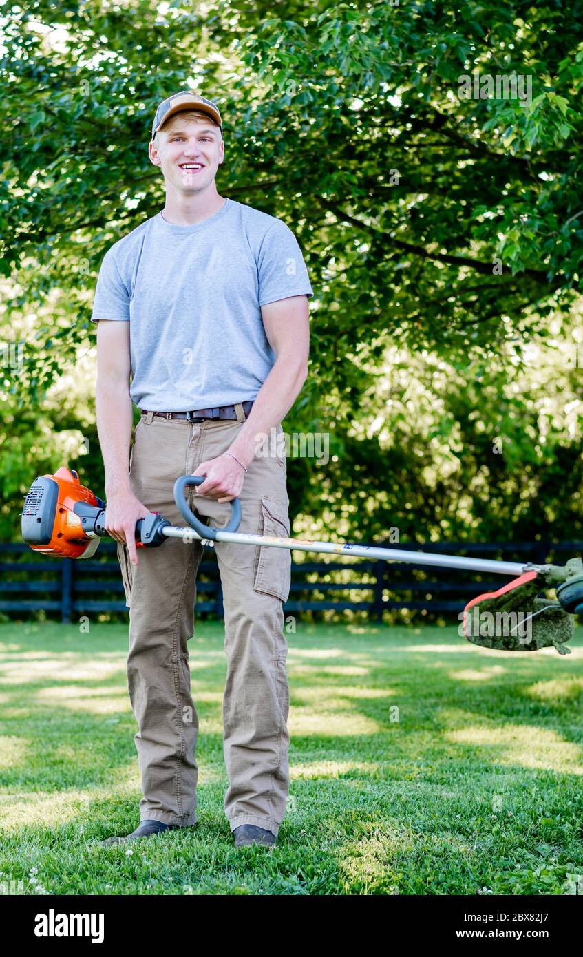 giovane uomo sorridente che indossa cappello che tiene mangiatore di erbacce Foto Stock