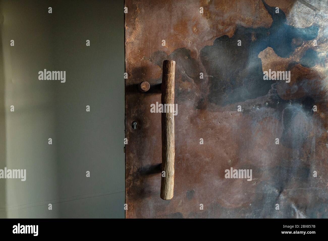 La porta in metallo molto ruvida e arrugginita ha una lunga maniglia rustica in legno. Foto Stock
