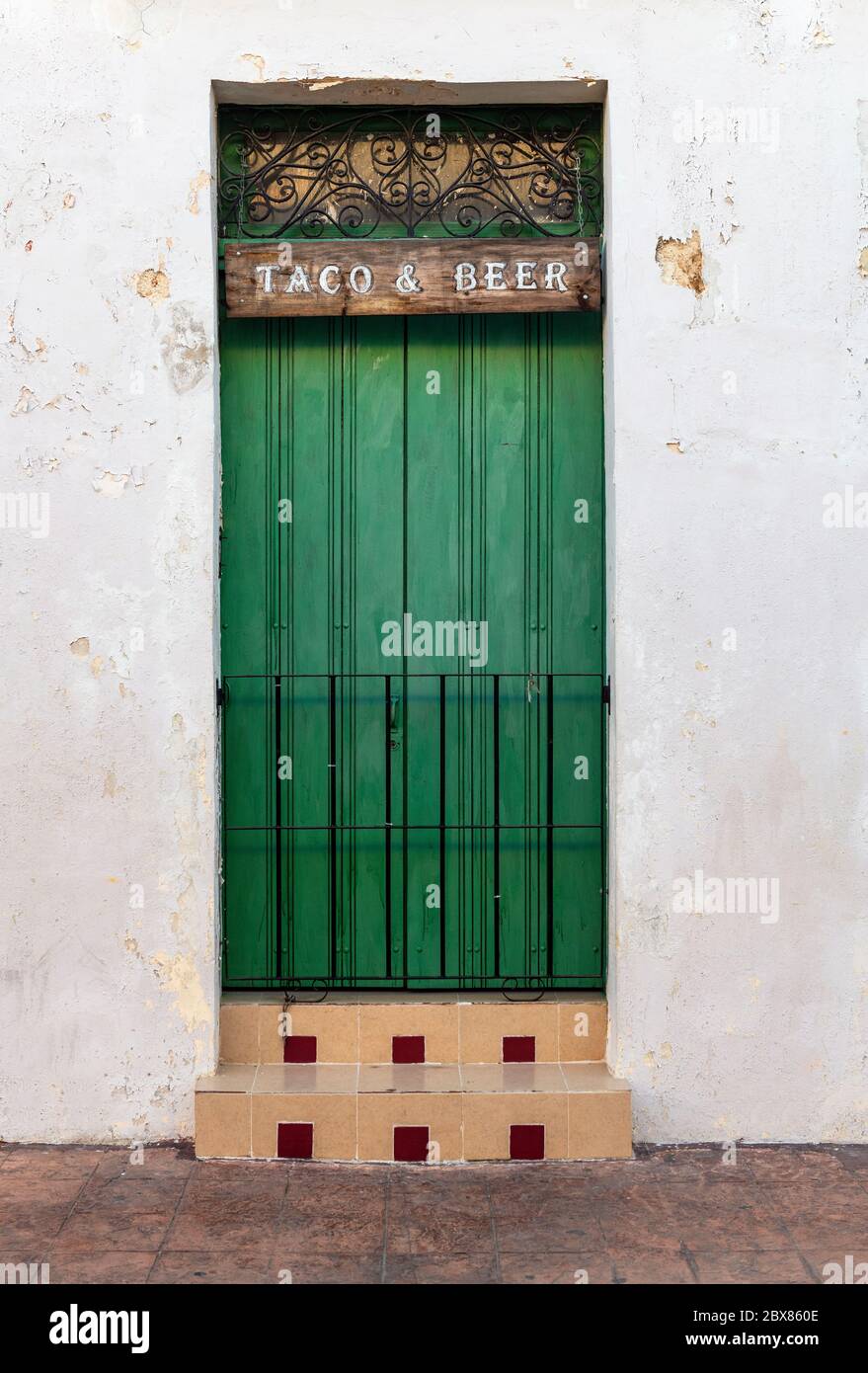 Facciata bianca in stile coloniale con porta metallica verde e un cartello 'Taco and Beer', Campeche, Messico. Foto Stock