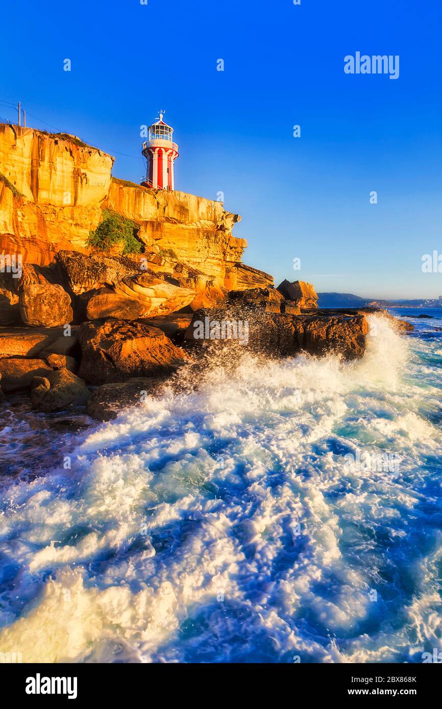 Faro Hornby bianco-rosso all'ingresso del porto di Sydney dall'oceano Pacifico in morbida luce mattutina contro il cielo blu chiaro. Foto Stock