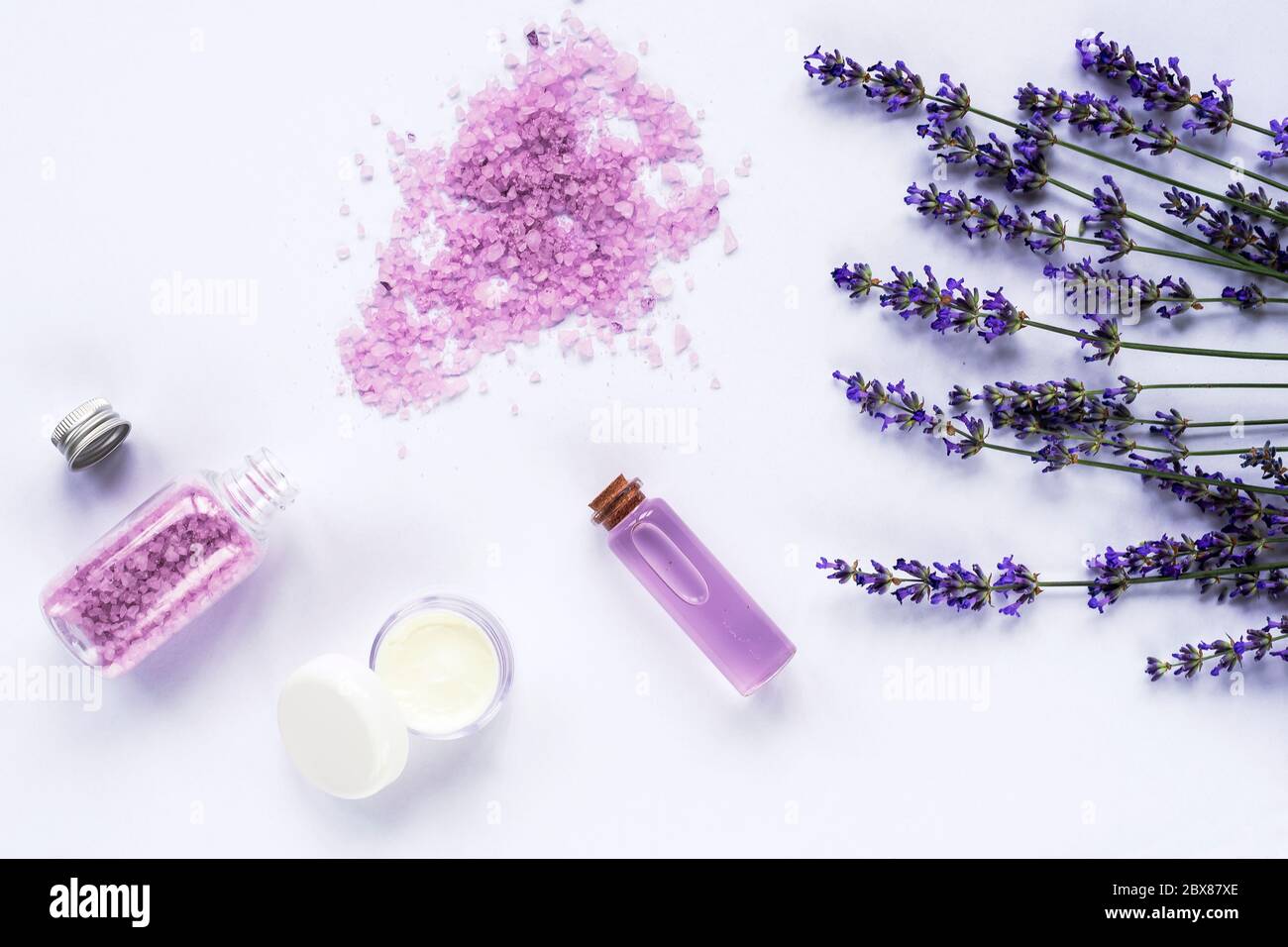 Fiore di lavanda, sale marino, vasetto di crema e olio essenziale su sfondo bianco, vista dall'alto, piatto. Foto Stock