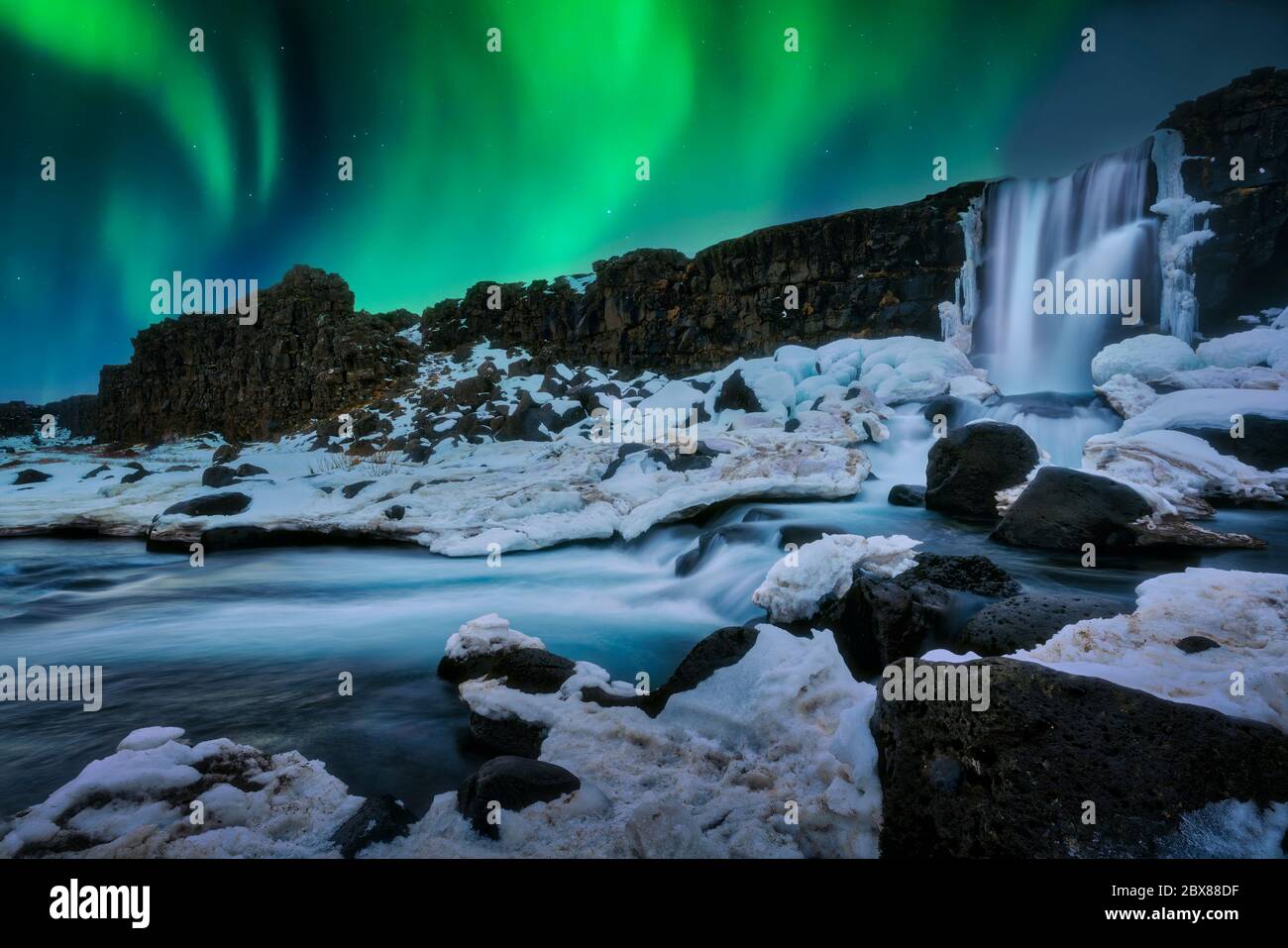 Inverno luci settentrionali sulla cascata Öxarárfoss in Islanda con un primo piano innevato. Foto Stock