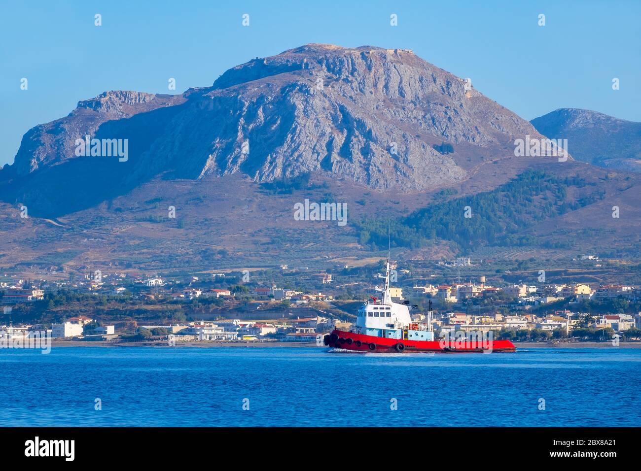 Giornata estiva soleggiato nel golfo di Corinto. Vista dall'acqua al tugboat sullo sfondo di una piccola cittadina su una riva montagnosa Foto Stock