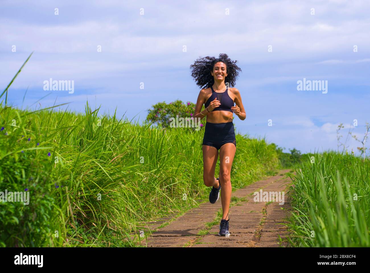 happy femminile runner formazione su strada campagna - giovane attraente e in forma jogger donna facendo l'allenamento in esecuzione all'aperto su bella pista in salute Foto Stock