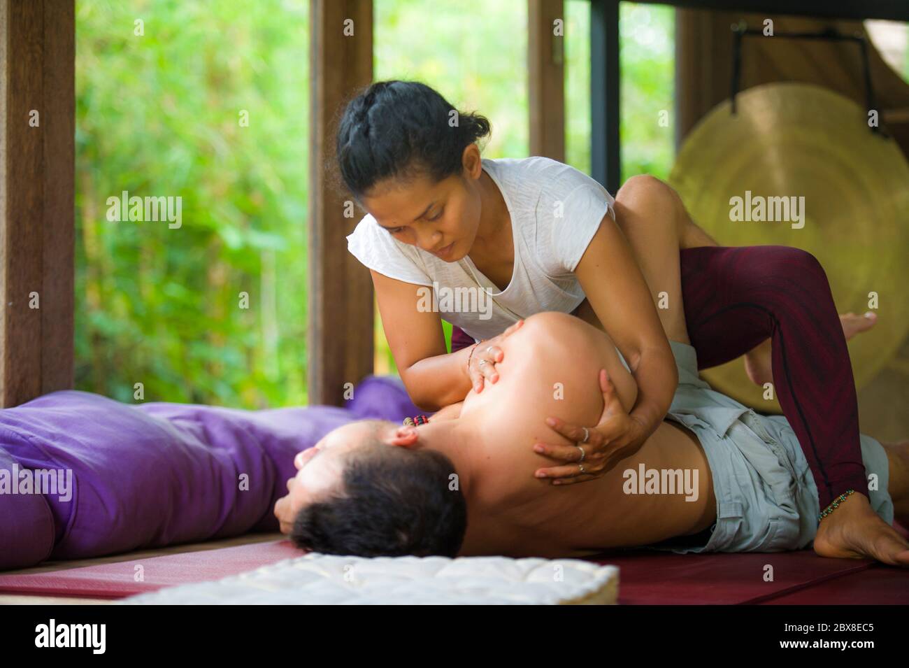 Giovane bella ed esotica donna terapista indonesiana che offre massaggio tradizionale tailandese per l'uomo disteso in relax presso spa tropicale benessere in salute n Foto Stock