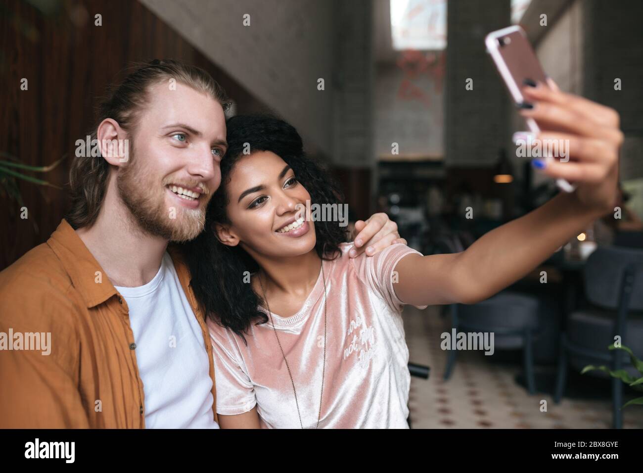 Giovane coppia fresca che fa foto sulla fotocamera frontale del cellulare in ristorante. Bella donna afroamericana facendo foto con un amico in caffetteria. Frate sorridenti Foto Stock
