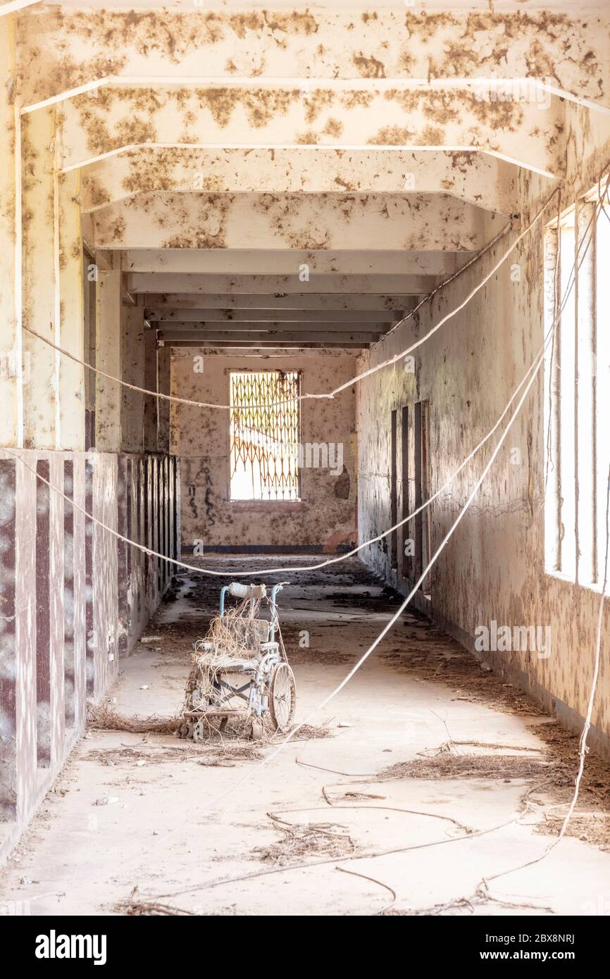 Una sedia a rotelle coperta di polvere nel corridoio abbandonato di un edificio abbandonato, spazio copia, nessuna gente Foto Stock