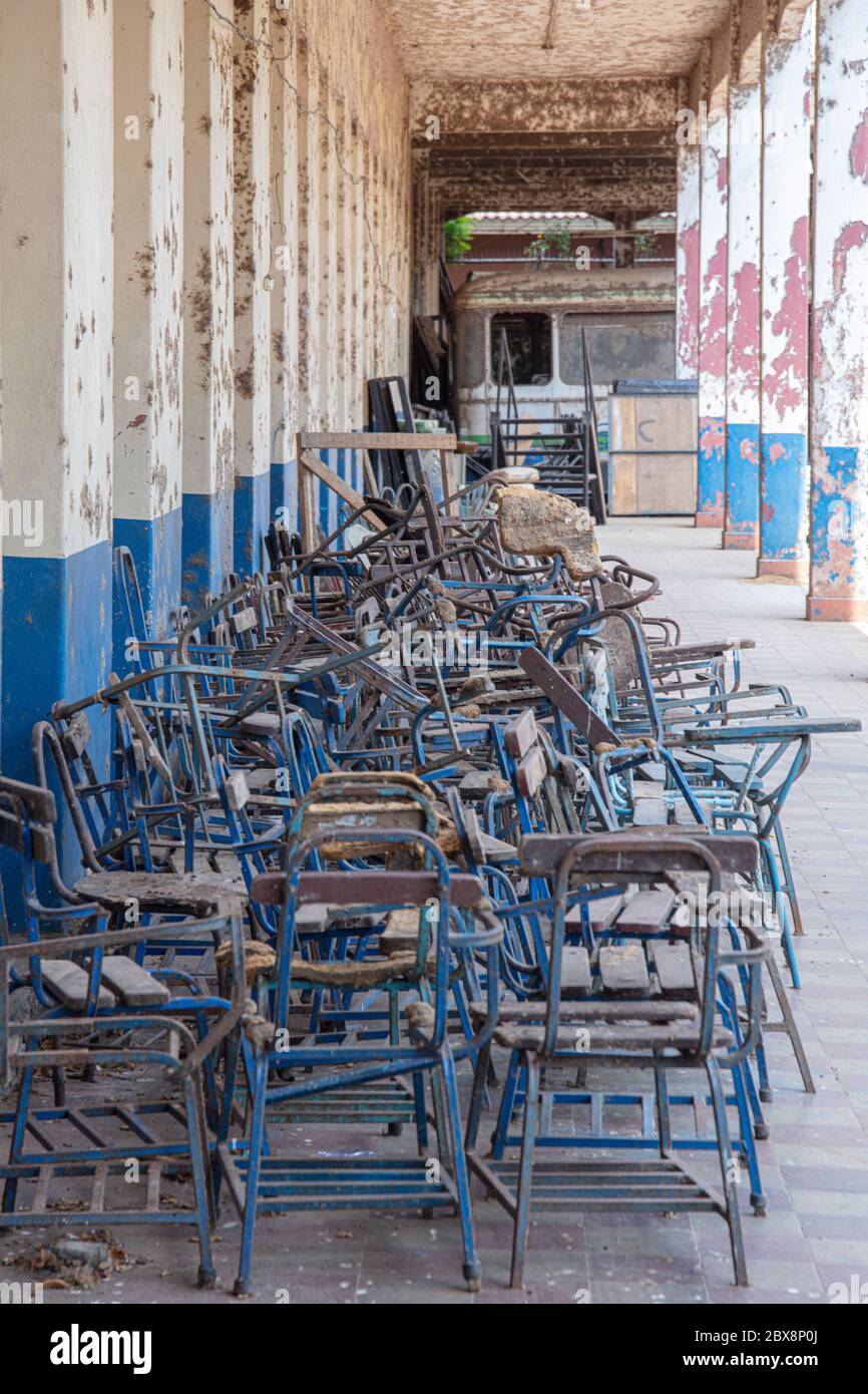 Una scuola superiore abbandonata: Vista lungo un corridoio esterno di sedie polverose verso un bus scolastico abbandonato, la fine della scena mondiale Foto Stock